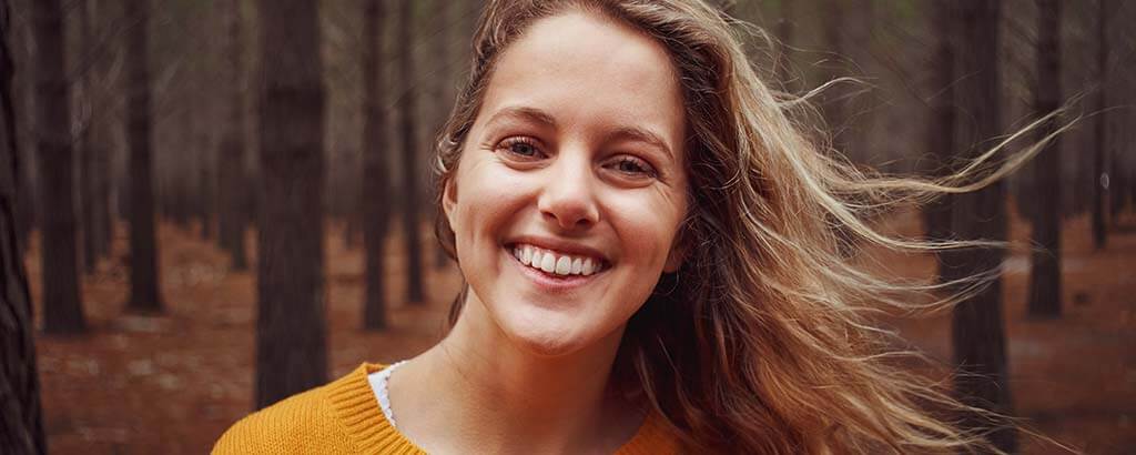 a woman smiles in the woods after receiving general dentistry